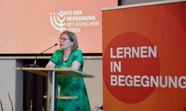 Dr. Ulrike Offenberg an einem Rednerpult, im Hintergrund Plakat und Logo von Orte der Begegnung