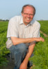Bild von Rainer Carstens, er kniet auf einem Möhrenfeld, lächelt, er trägt Jeans und ein kurzärmeliges Hemd.